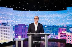 a man standing at a podium in front of a large screen with buildings on it