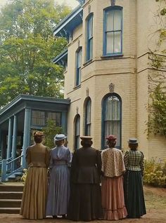 four women standing in front of a large house with steps leading up to the porch