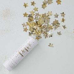 a white tube filled with gold stars on top of a white table next to confetti