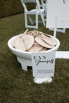 a white bowl filled with paper leaves on top of a grass covered field next to chairs