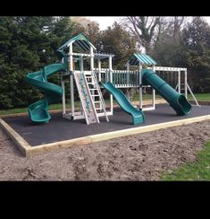 a green and white play set in the middle of a field with trees behind it