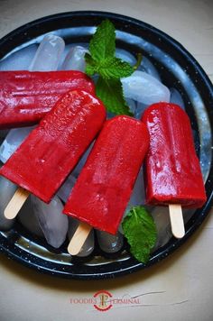 three popsicles with mint leaves on them in a black bowl next to ice cubes