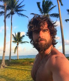 a man with long hair and beard standing in front of palm trees on the beach