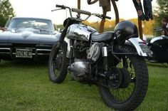 a motorcycle parked on top of a lush green field next to other cars and people