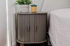 a small cabinet next to a bed with a plant on top and a potted succulent in the corner