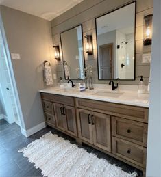 a bathroom with double sinks and mirrors on the wall, along with a white rug