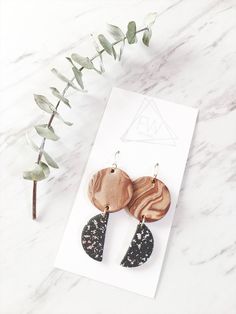 two wooden earrings with black and white speckles on them next to a plant