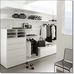 a white closet filled with lots of clothes and bags on top of shelves next to a window