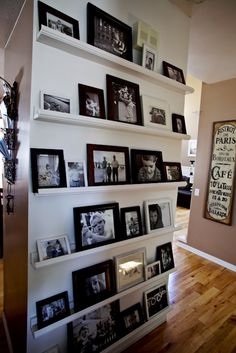 a wall filled with lots of pictures and framed photos next to a wooden floor in a living room