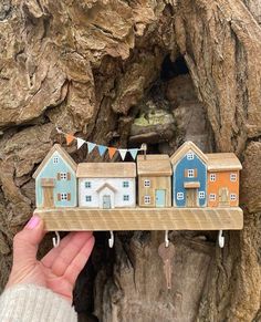 a hand holding a small wooden toy house on a tree branch with bunting flags