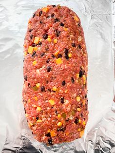 an uncooked meatloaf covered in corn and black beans on aluminum foil