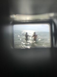 the reflection of two surfers in the water from inside a camera flash lens on a surfboard