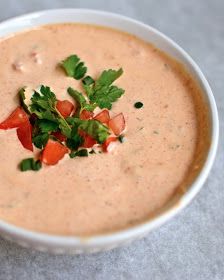 a white bowl filled with soup and garnished with cilantro, parsley and tomatoes