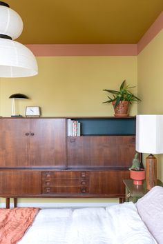 a bedroom with a bed, dresser and lamp on the wall above it in front of two hanging lights