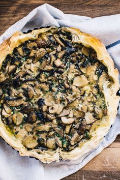 a mushroom and spinach quiche on a wooden table with a white towel next to it