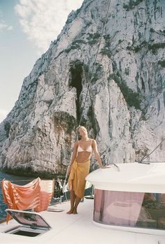 a woman in a bathing suit standing on the deck of a boat near a mountain