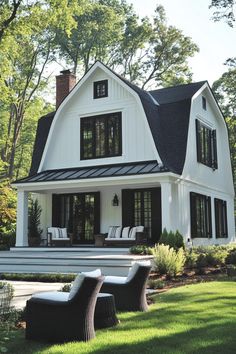 a white house with black shingles on the roof and two lawn chairs in front