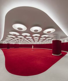 a person standing in the middle of a room with red carpet and round lights on the ceiling