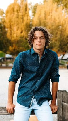 a young man leaning on a wooden fence with his hands in his pockets and looking at the camera