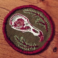 a patch with a deer's skull and pine needles in the center on a wooden surface