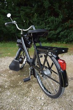 a black bicycle parked on top of a gravel road next to trees and bushes in the background