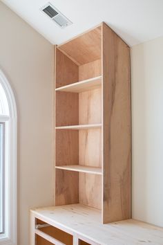 an empty wooden shelf in the corner of a room next to a window with white trim