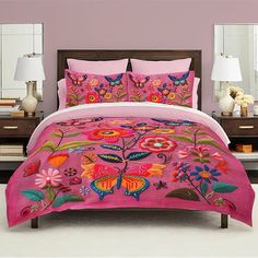 a bed covered in pink comforter and pillows with butterflies on the sheets, along with two lamps