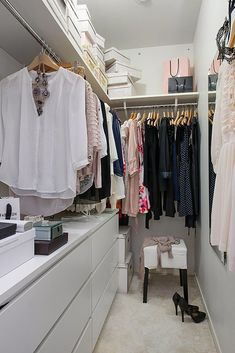 a walk in closet with clothes hanging on the wall and a stool next to it