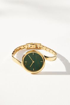 a gold wrist watch with green face on a white surface, taken from the front