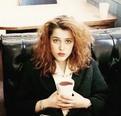 a woman sitting in a chair holding a cup of coffee and looking at the camera