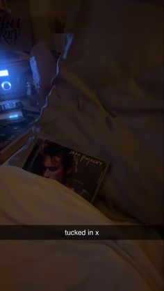 a person laying in bed with their head on the pillow and holding an album next to them