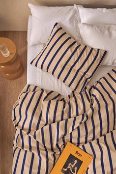 a bed with blue and white striped sheets on top of it next to a yellow book