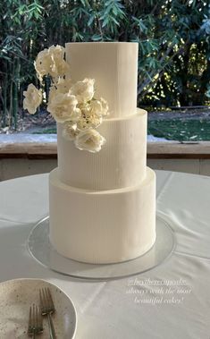 a three tiered cake with white flowers on the top is sitting on a table