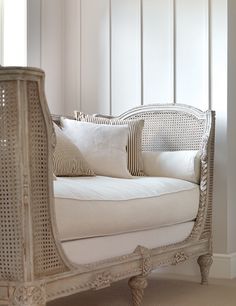 a white wicker couch with pillows on it in front of a wall and window