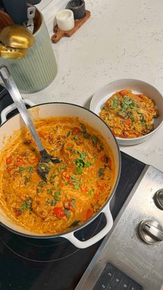 a large pot filled with food sitting on top of a stove next to two bowls