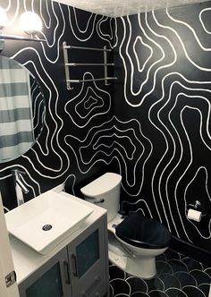 a bathroom decorated in black and white with an interesting pattern on the wall behind the toilet