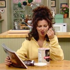 a woman sitting at a table eating cereal and reading a newspaper with a coffee mug in front of her