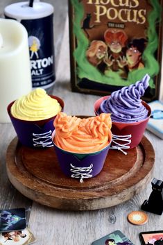 three cupcakes with frosting on a wooden tray next to some books and candles