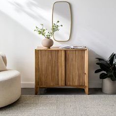 a room with a chair, mirror and plant on the sideboard next to it