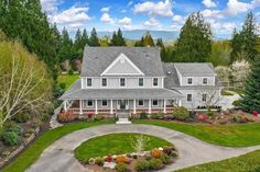 a large white house surrounded by trees and flowers in the middle of a lush green yard