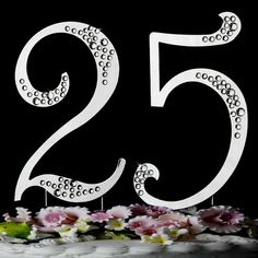 a white cake topped with a large number twenty five birthday cake topper next to pink flowers