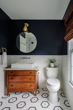 a white toilet sitting next to a wooden dresser in a bathroom under a round mirror