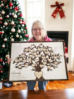 an older woman holding up a family tree sign in front of a decorated christmas tree