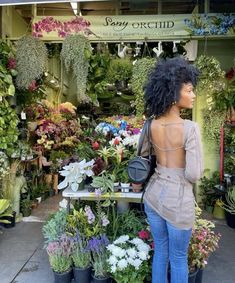 a woman standing in front of a flower shop with lots of plants and flowers on display