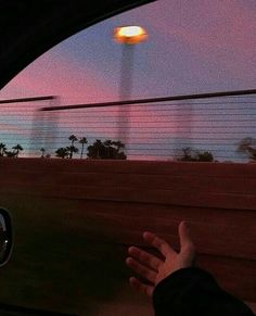 a person's hand out the window of a car as the sun is setting