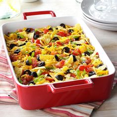 a red casserole dish with black olives, tomatoes, and tortilla chips