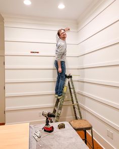 a man is standing on a ladder in the middle of a room with white walls