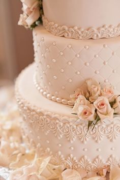 a three tiered white wedding cake with pink roses on the side and pearls around the edges