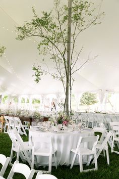 an outdoor tent with tables and chairs set up for a wedding reception under a tree