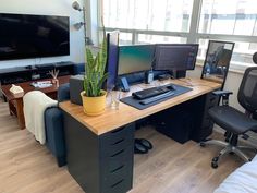 a desk with two monitors and a keyboard on it in front of a large window